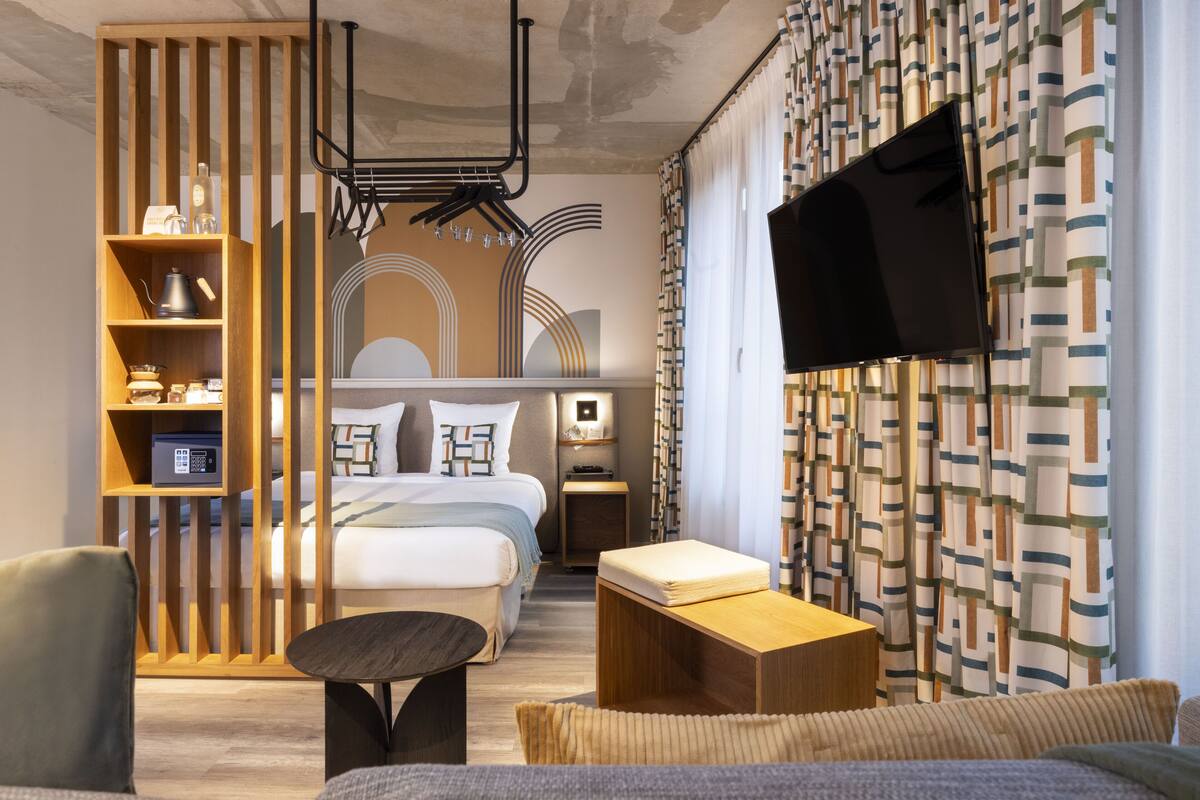 A modern hotel room with a bed, a TV, a wooden sideboard, and a small table.
