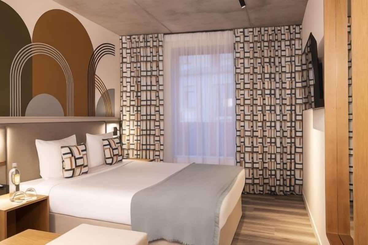 A modern hotel room with a bed, bedside tables, a mirror, and patterned curtains.