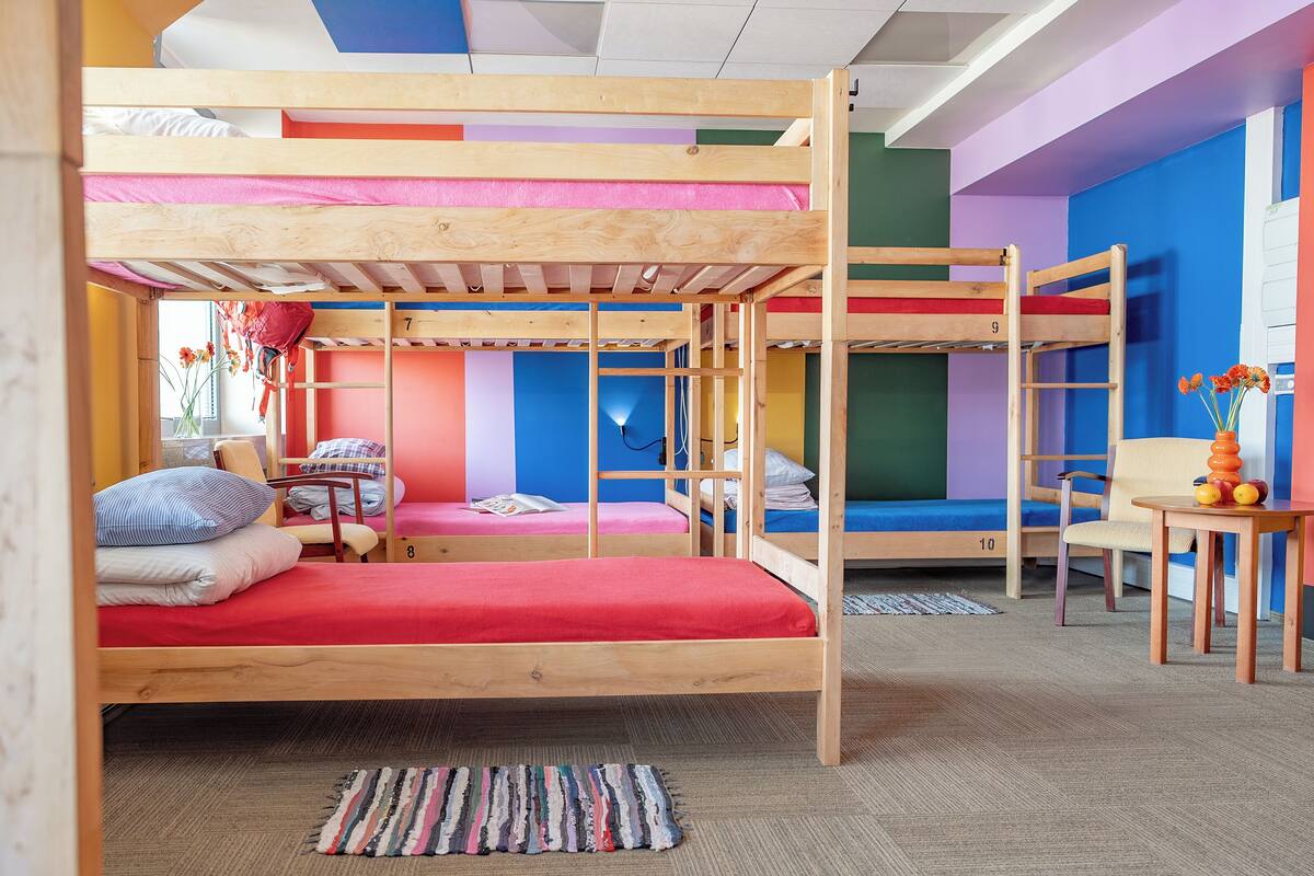 A bunk bed room with a wooden frame, a red mattress, and a striped rug on the floor.