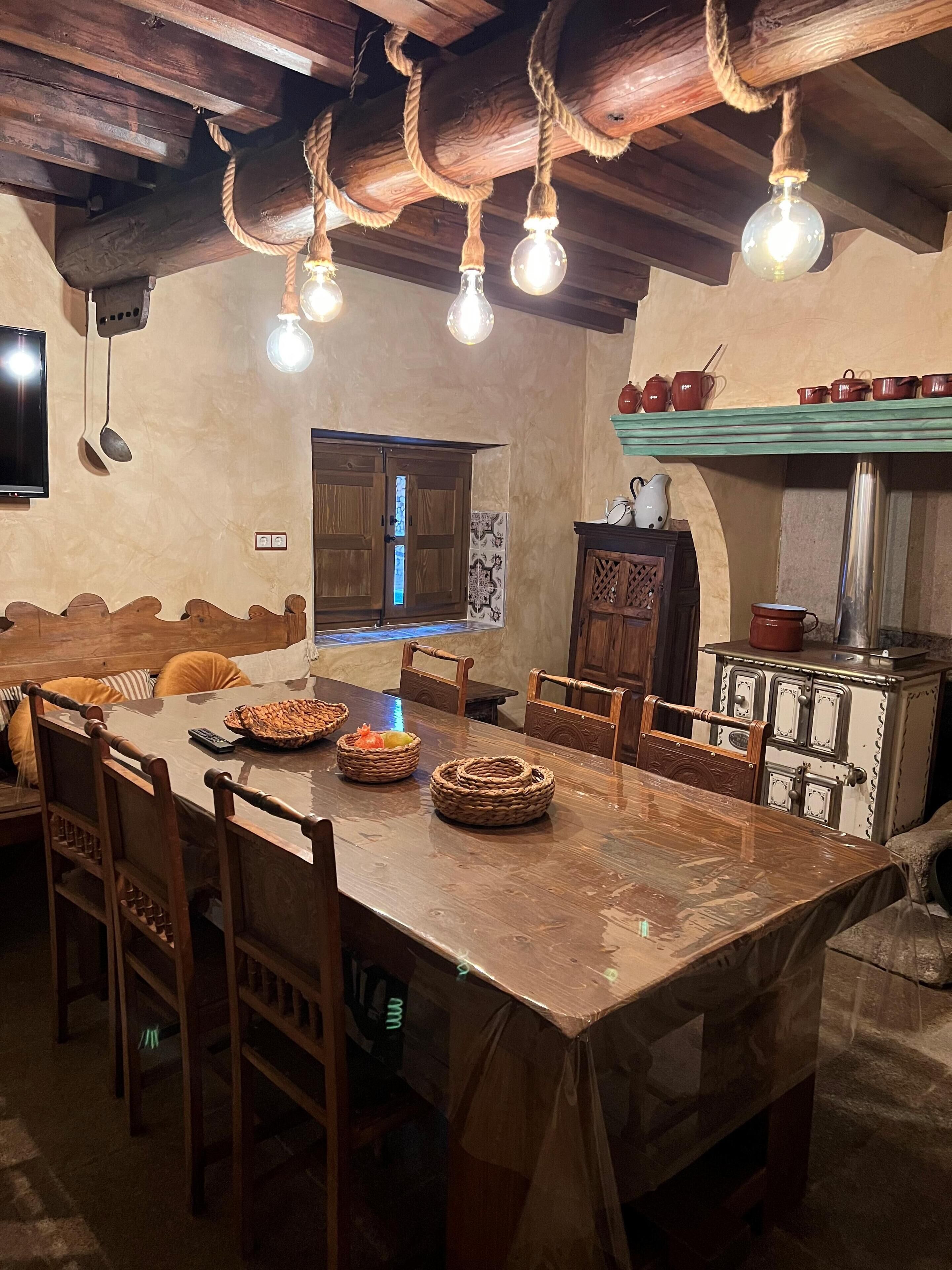 Uma área de jantar rústica com mesa de madeira, cadeiras e um lustre.