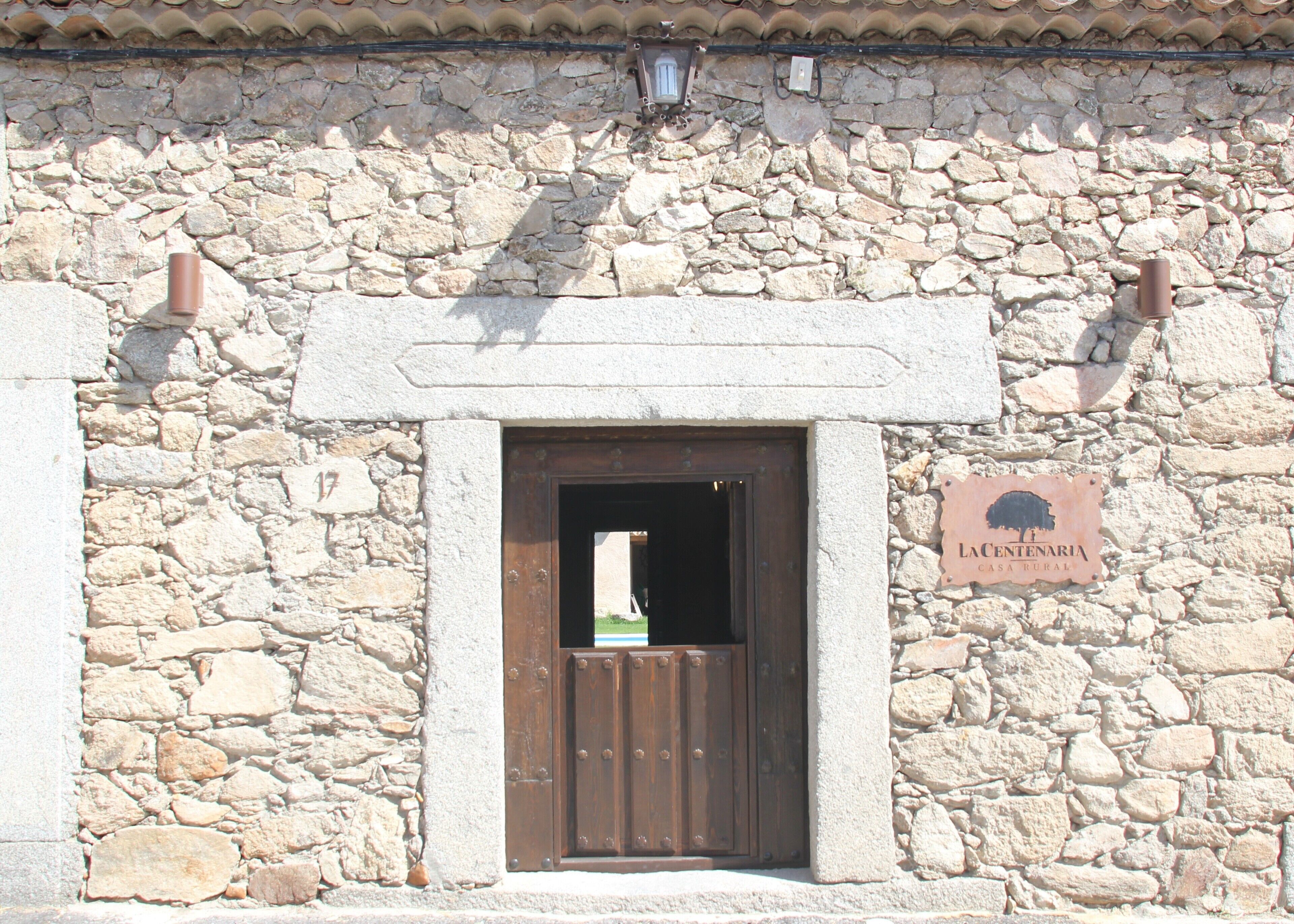 A rustic stone building with a wooden door and a sign reading "LA CENTENARIA CASA RURAL".