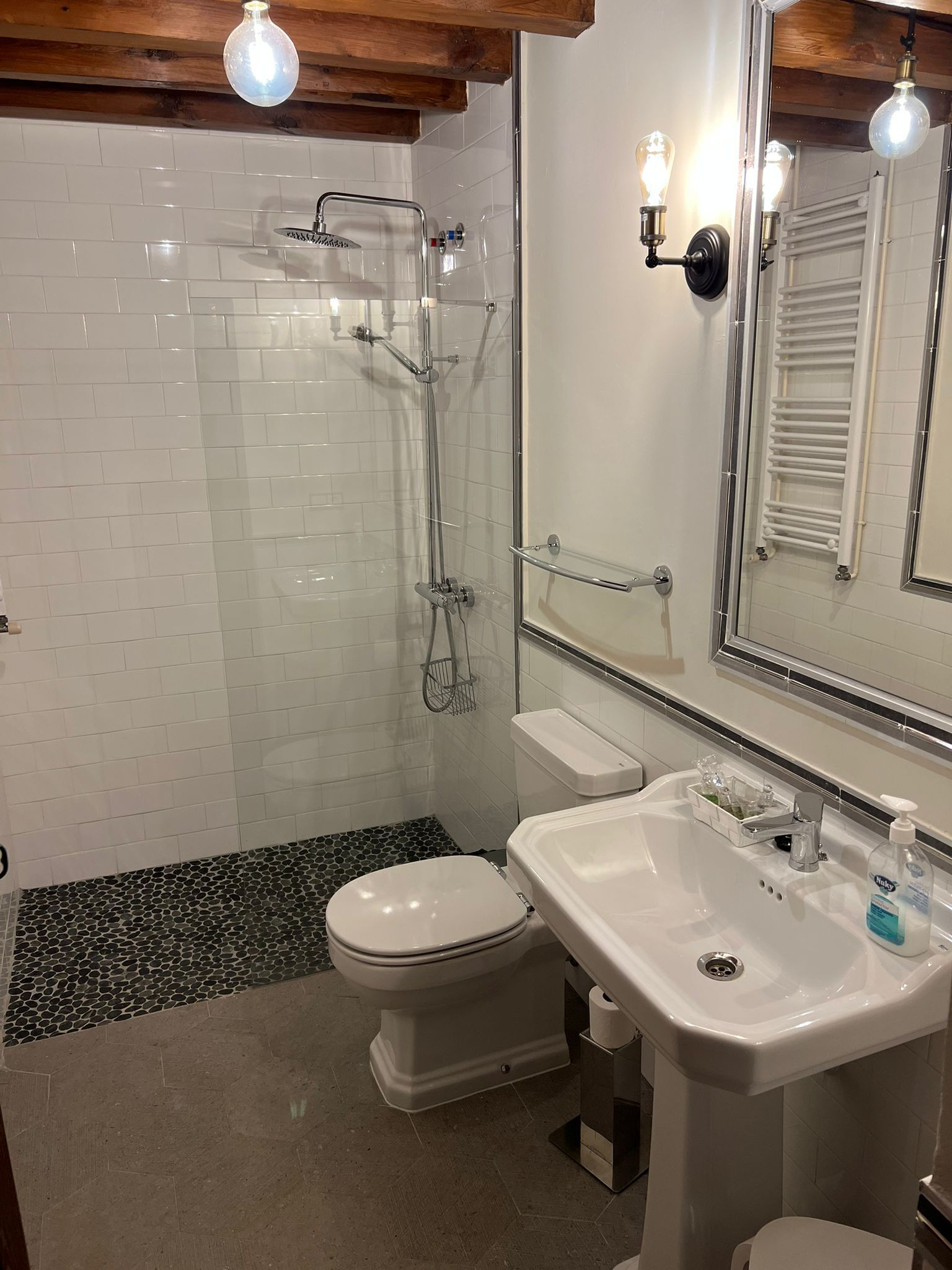 Un baño moderno con ducha de vidrio, inodoro blanco y lavamanos con espejo.