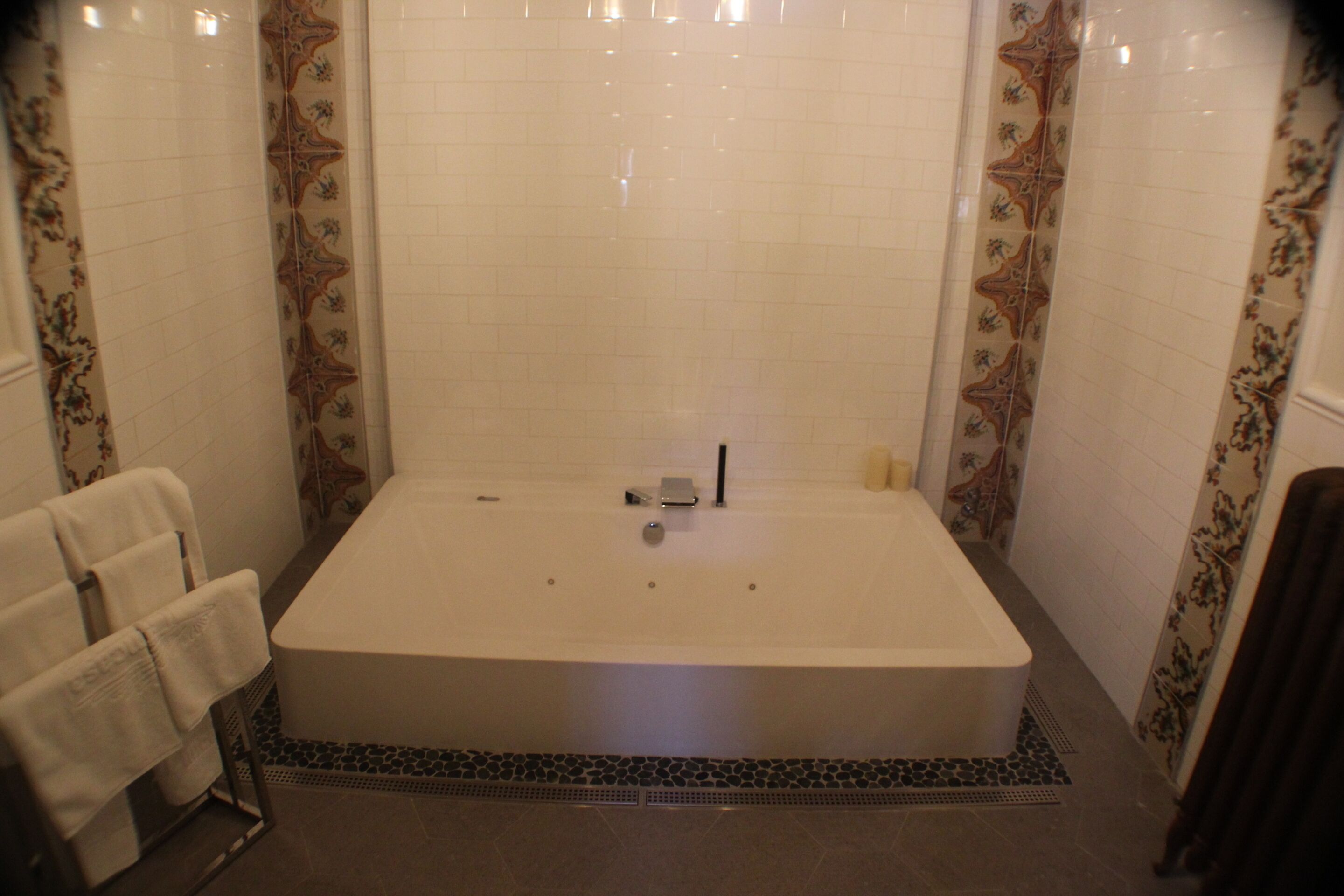 Un baño con una bañera grande, paredes de azulejos y un borde decorativo.