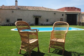 Dos sillas de mimbre frente a una piscina, con un edificio de piedra al fondo.