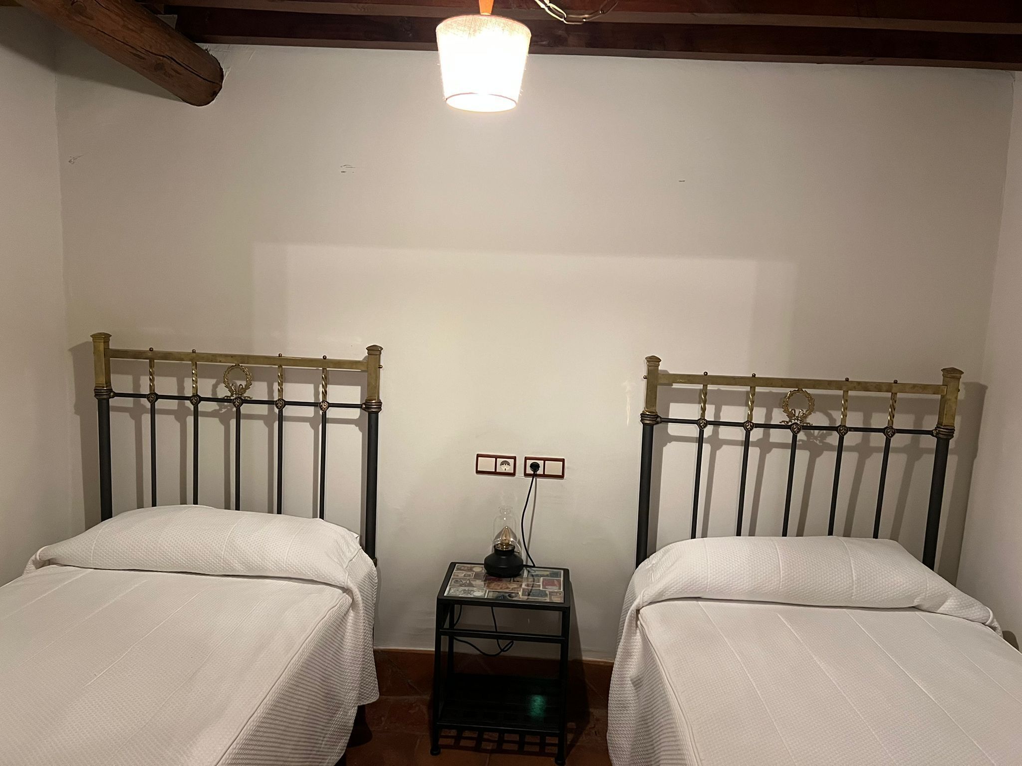 Una habitación con dos camas individuales, una mesita con una lámpara y un enchufe.