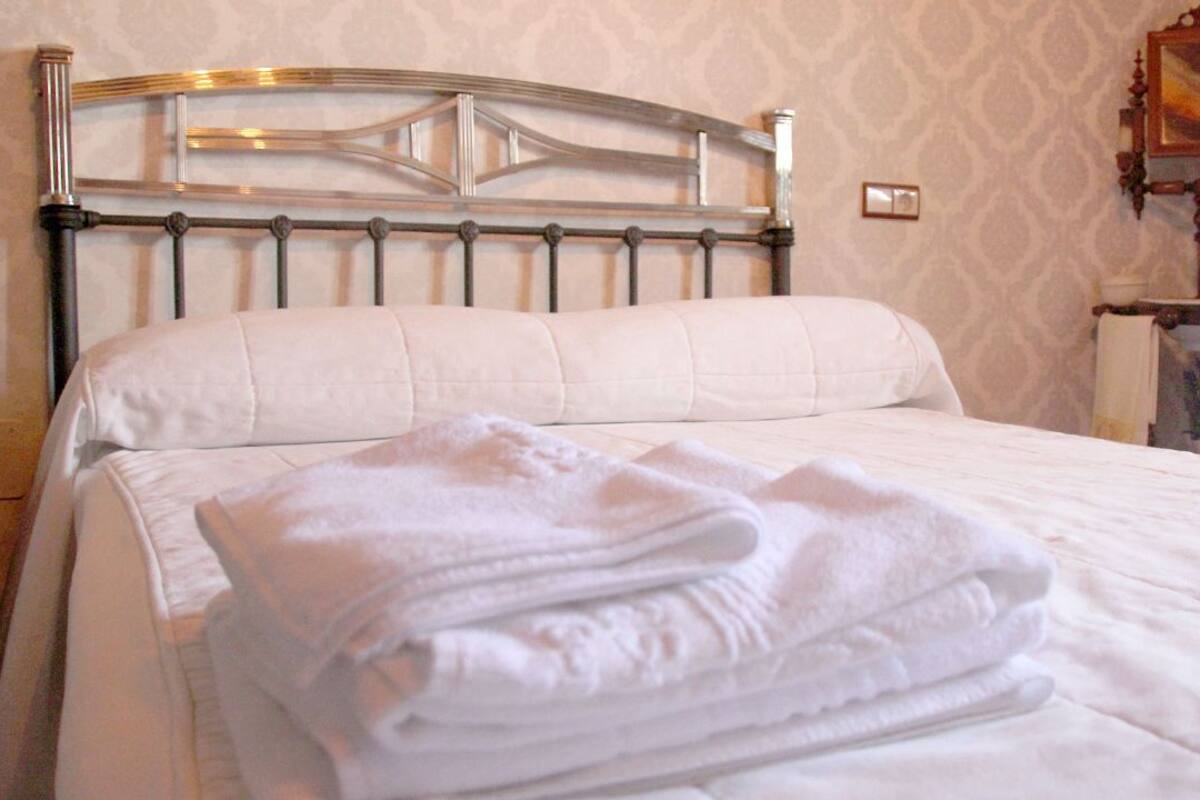 A neatly made bed with a metal headboard and a folded white towel on top.