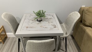 Ein kleiner Essbereich mit einem weißen Tisch und zwei Stühlen, einer Topfpflanze und einem beigen Sofa im Hintergrund.