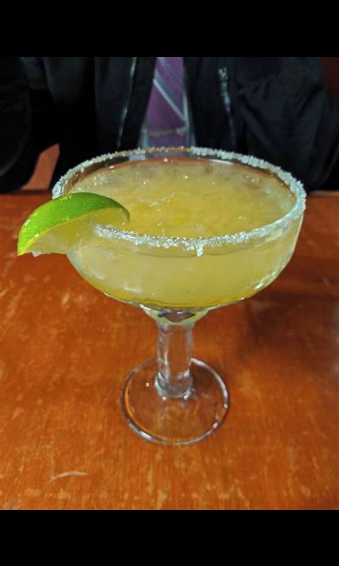 A margarita with a salted rim and a lime wedge on a wooden table.