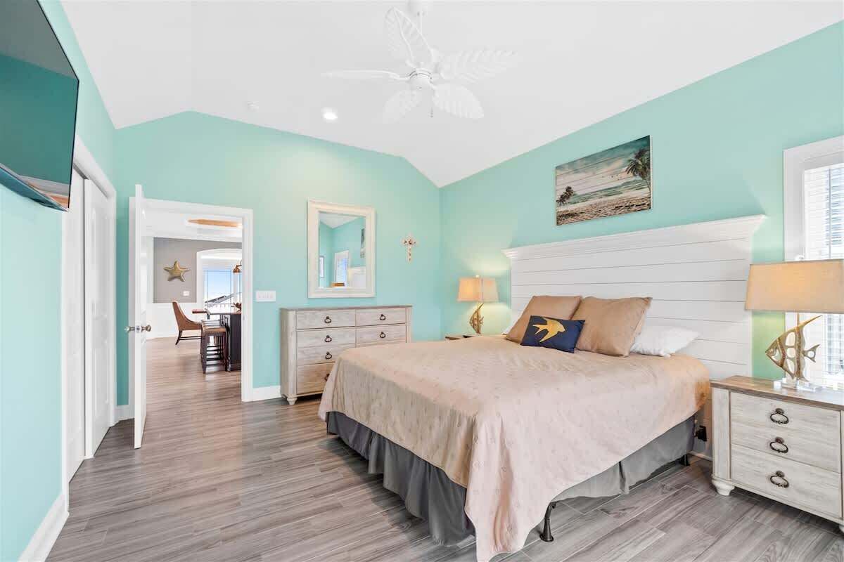 A bedroom with a bed, nightstands, a dresser, a ceiling fan, and a painting on the wall.
