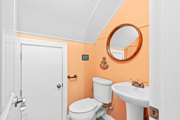A bathroom with a white toilet, a sink, and a mirror. - Beach Easy by Brunswick Vacation Rentals: Heated Pool & Spa, Tiki Bar, Elevator (Ocean Isle Beach)