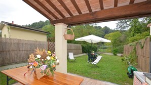 A wooden table with a floral centerpiece, a white umbrella, and outdoor seating. - Casa D'amelia (Camaiore)