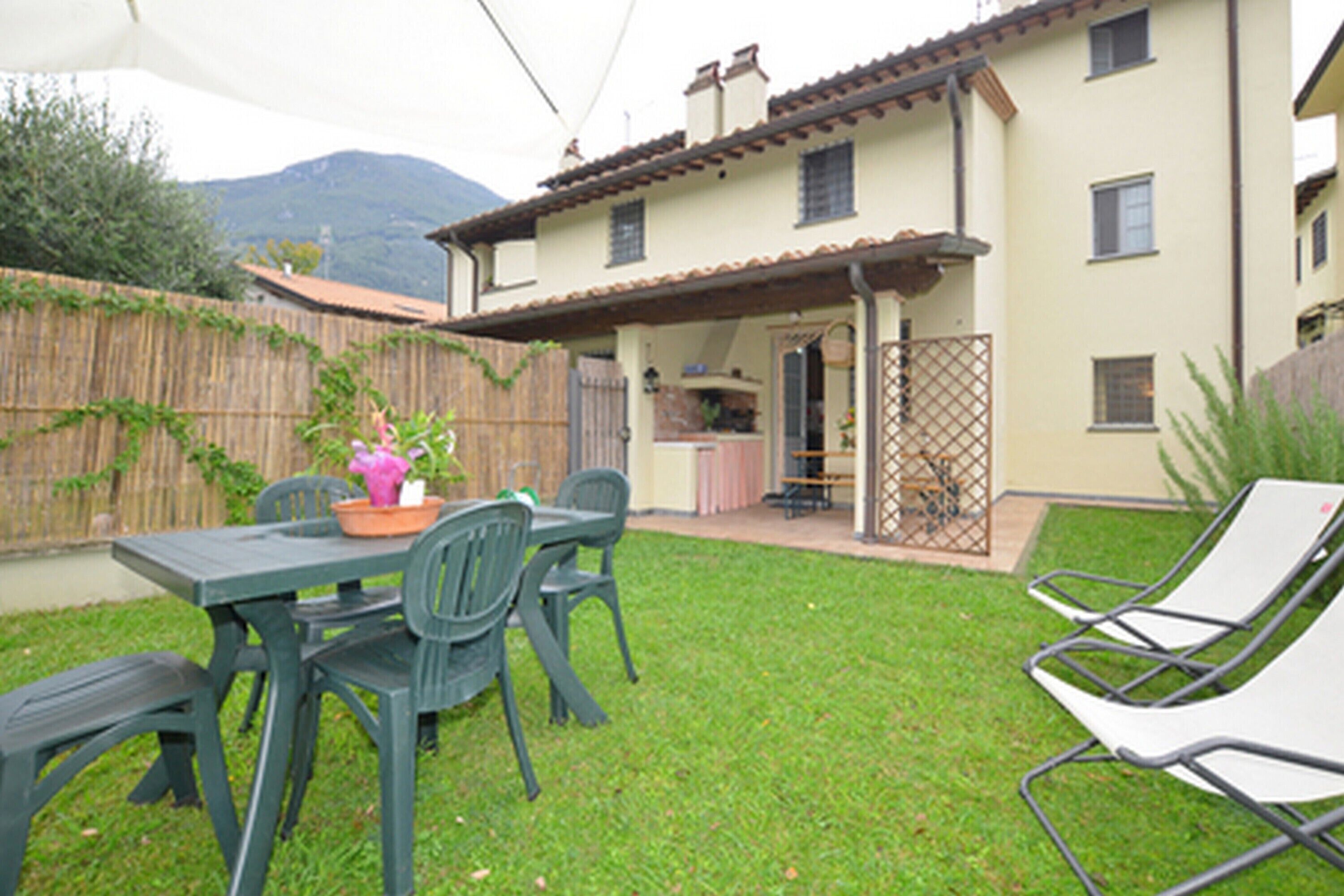 Un espace extérieur aménagé avec une table et des chaises, un coin salon abrité et une vue sur une montagne en arrière-plan.