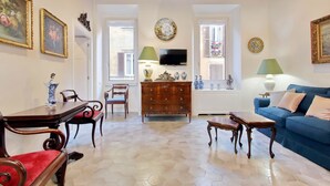 A living room with a wooden table, chairs, a blue sofa, and a TV on the wall. - Luxury apartment in Rione Monti (Roma)