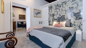 A bedroom with a bed, a chair, a door, a painting, and a wall with a textured design. - Luxury apartment in Rione Monti (Roma)