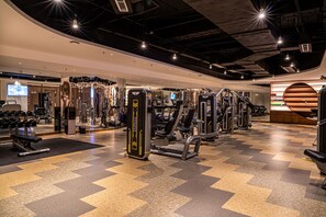 Een moderne sportschool met diverse fitnessapparaten, een spiegelwand en een geruite vloer.