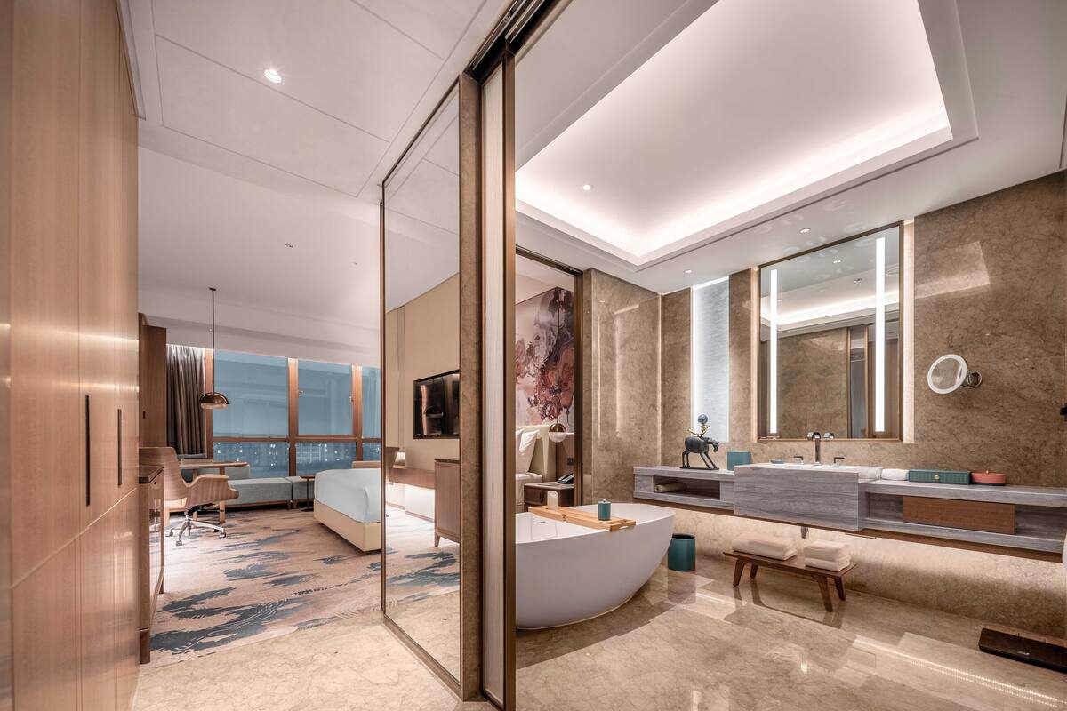 Une chambre d’hôtel moderne dotée d’une grande baignoire à formes arrondies, d’un grand miroir et offrant une vue sur la ville.