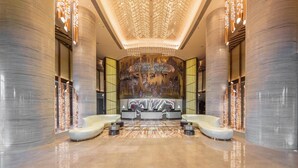 Un hall d’entrée luxueux, orné de colonnes en marbre, doté d’un comptoir d’accueil et d’un lustre moderne.