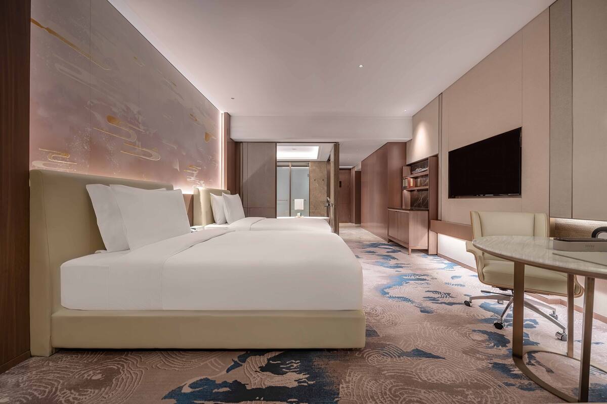 Une chambre d’hôtel avec un grand lit, un bureau, une chaise, une télévision et une grande fenêtre.
