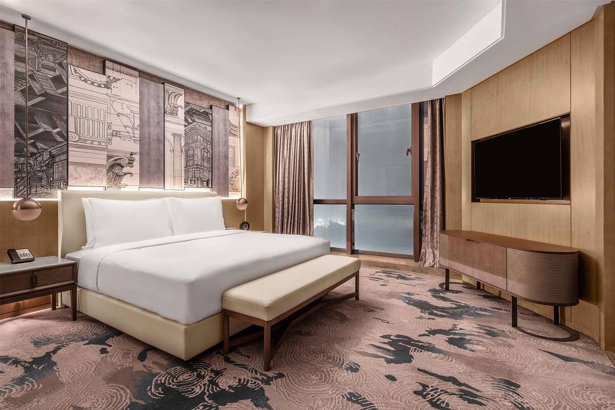 Une chambre d’hôtel avec un grand lit, un banc, une télévision et une grande fenêtre.