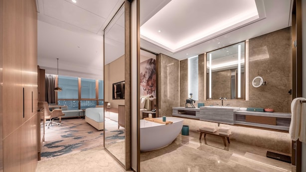 Une chambre d’hôtel moderne dotée d’une baignoire à formes arrondies, d’un grand miroir, d’un coin salon et offrant une vue sur la ville.