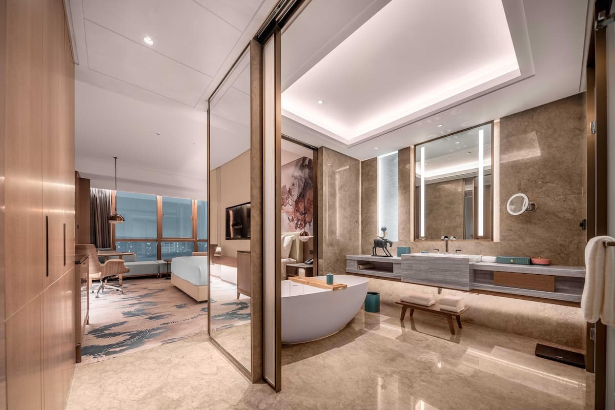 Une chambre d’hôtel moderne dotée d’une baignoire à formes arrondies, d’un grand miroir, d’un coin salon et offrant une vue sur la ville.