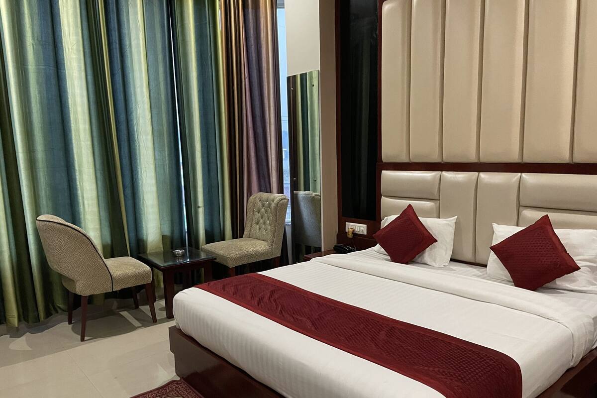A hotel room with a large bed, two chairs, a desk, and a red carpet.