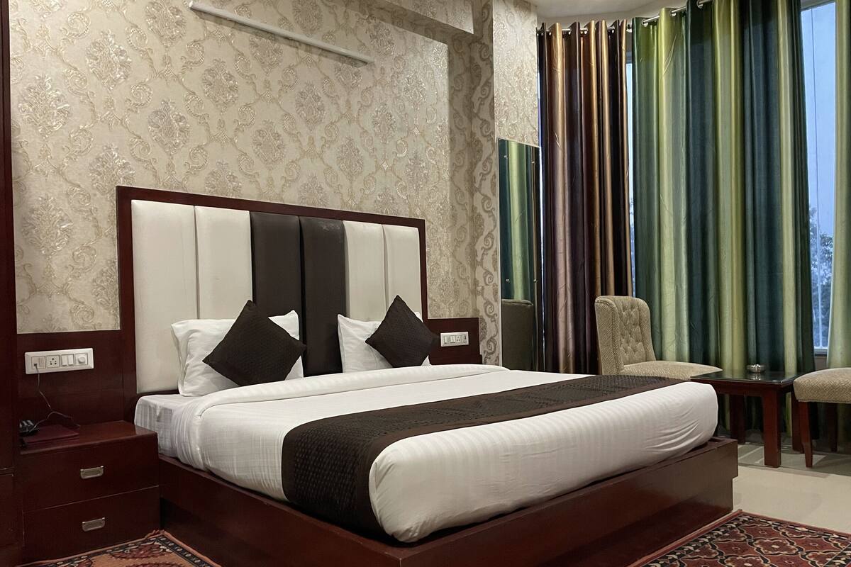 A hotel room with a large bed, a wooden nightstand, a chair, and a patterned rug.
