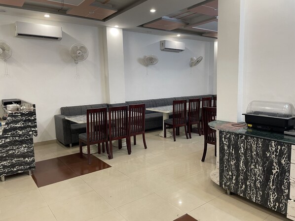 A modern dining area with a marble countertop, wooden chairs, a grey sofa, and built-in ceiling fans. - Sumedha G Village Resort and Spa (Yamkeshwar)