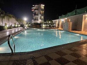 Une piscine nocturne avec un bord carrelé, une échelle en métal et un mur de pierre surmonté d’un pilier en pierre.