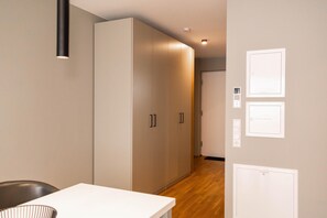 A hallway with a white table, a black chair, and a wardrobe. There are light switches and a door on the wall.