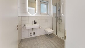 A modern bathroom with a white sink, toilet, and glass-enclosed shower. - Chic apartment - Überlingen on Lake Constance (Überlingen)