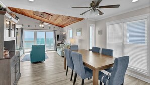 Una habitación amplia con techo de madera, una mesa de comedor con sillas, un sofá y un balcón con vistas.