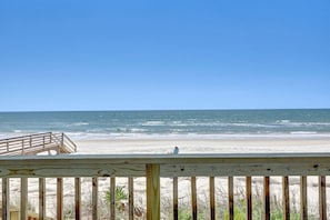 A beach view with a wooden deck and a person sitting on the sand.