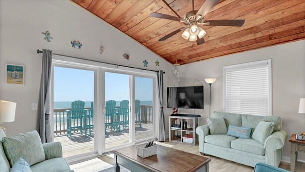 Una sala de estar con techo de madera, un televisor, un sofá y vista a la playa.