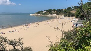 Ein Strand mit Menschen, die sonnenbaden und schwimmen, ein klarer Himmel und Gebäude im Hintergrund.