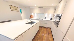 Une cuisine moderne avec des meubles blancs, un îlot central doté d’un évier et un plancher en bois.