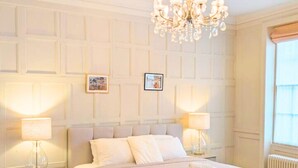 Une chambre d’hôtel avec un lit, deux lampes de chevet, un lustre et une fenêtre avec des stores.