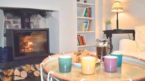 Un salon chaleureux avec une cheminée, une table basse ronde ornée de bougies, une bibliothèque et une lampe.