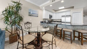 A modern kitchen with white cabinets, a glass-top dining table, and a large potted plant.