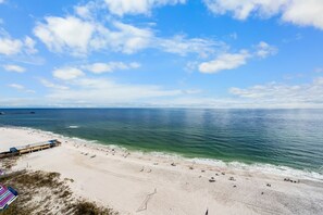 Een strand met een pier, heldere lucht en rustig water.