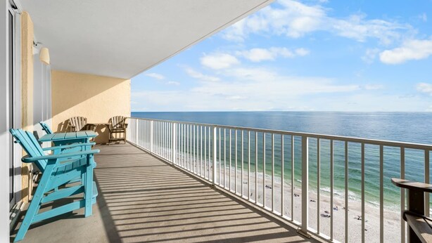 A balcony with a view of the ocean, featuring a railing, a table, and two chairs.
