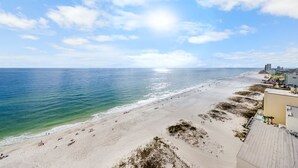 A beach with a clear sky, calm sea, and buildings along the shore.