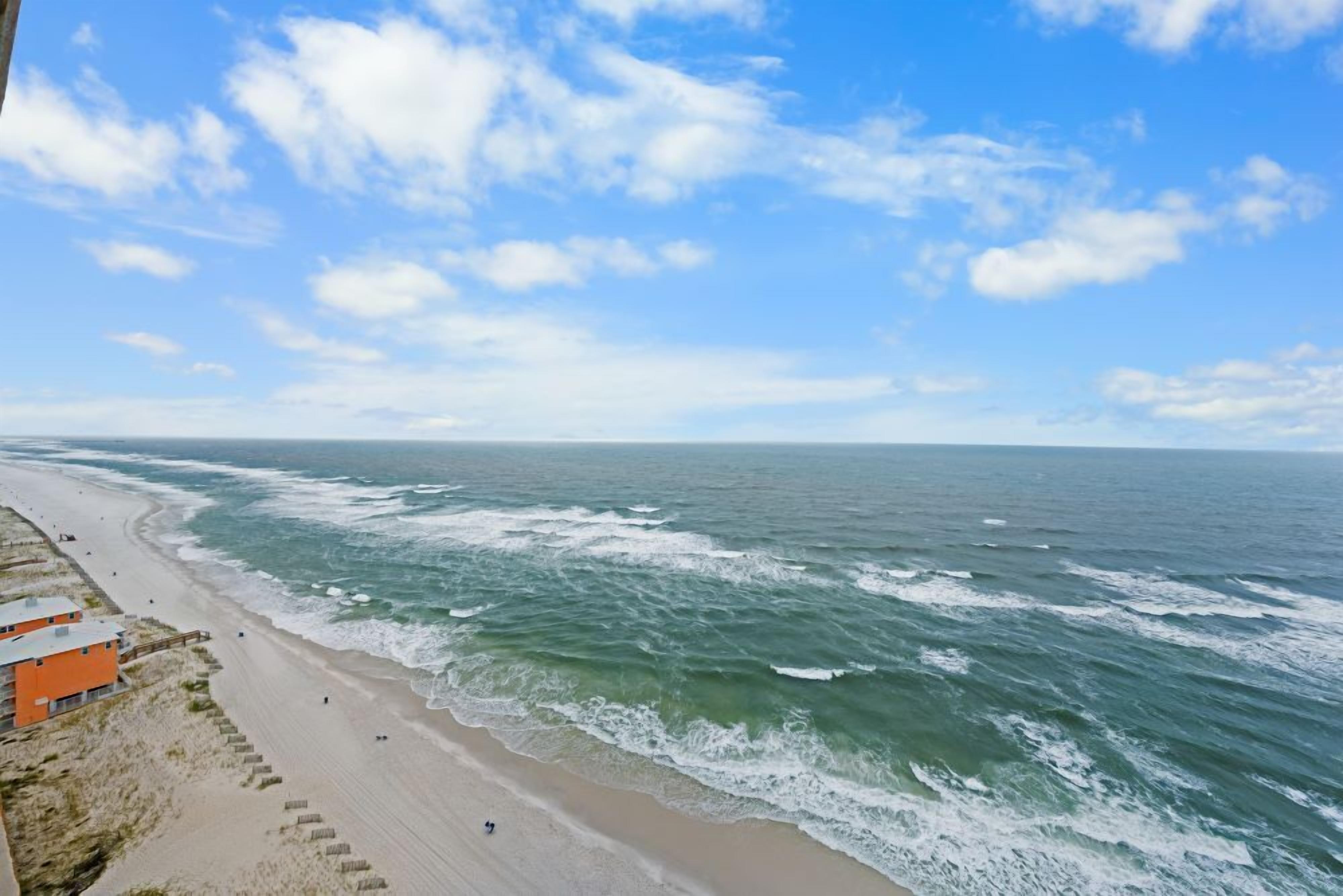 A beach with waves, a clear sky, and a building on the left.