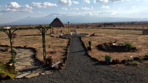 A rural landscape with a paved pathway leading to a central area with seating and a small structure. - Amanya Double Pitch Tent With Mt Kilimanjaro View (Amboseli)
