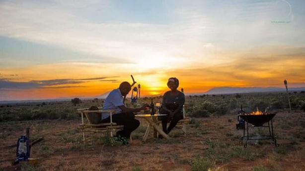 Two people sitting at a table outdoors with a sunset in the background. - Amanya Double Pitch Tent With Mt Kilimanjaro View (Amboseli)