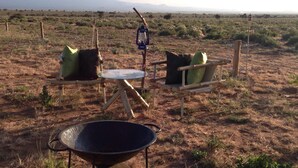 A rustic outdoor seating area with two chairs and a table, surrounded by dry grass and sparse vegetation. - Amanya Double Pitch Tent With Mt Kilimanjaro View (Amboseli)