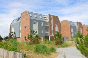 A modern residential building with a sloped roof, brick facade, and multiple windows. - Beachfront Vacation Apartment - LekkerNaarZee A203 (Callantsoog)