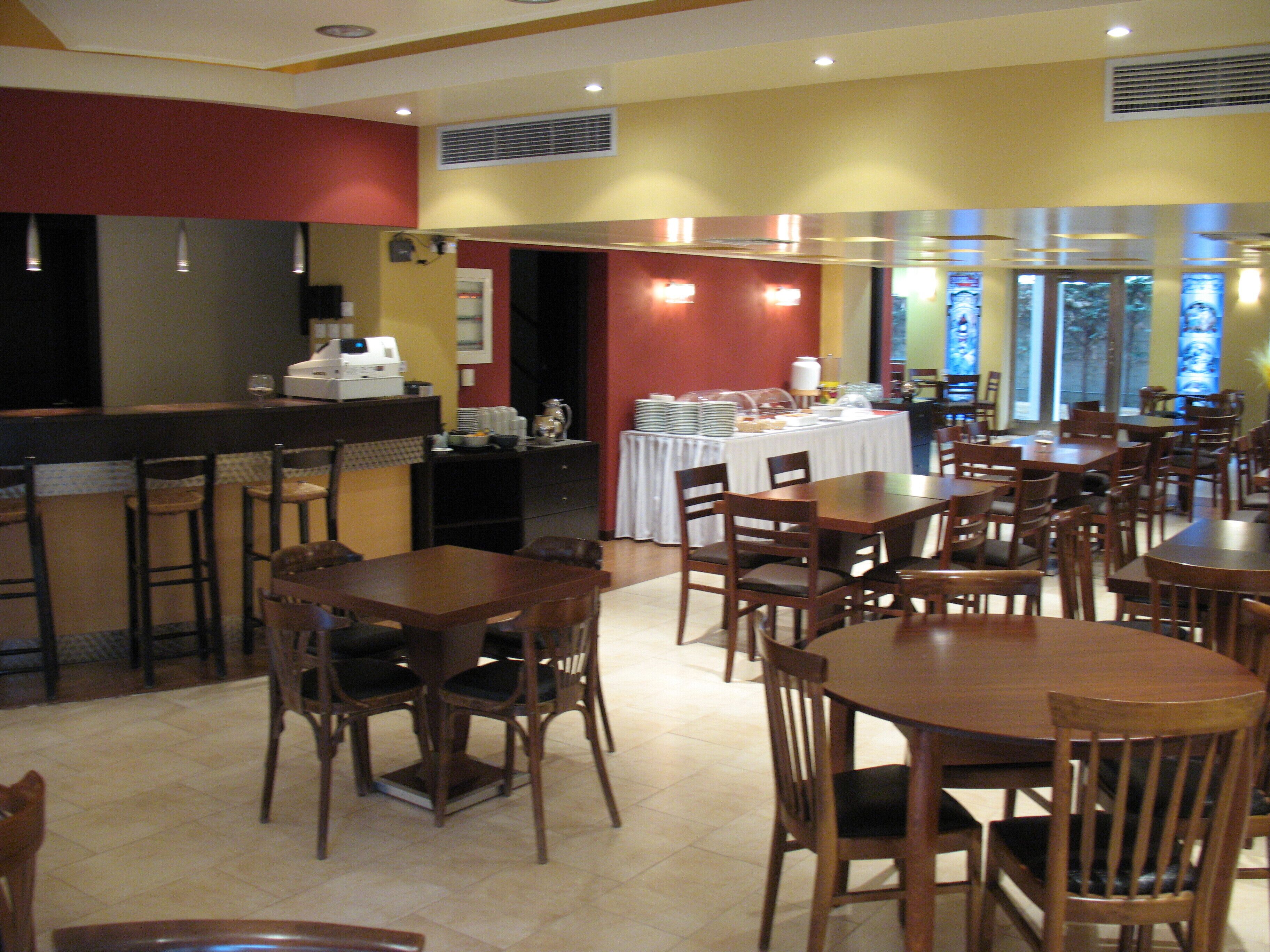 A restaurant with multiple wooden tables and chairs, a buffet area with food and drinks, and a counter with a coffee machine.