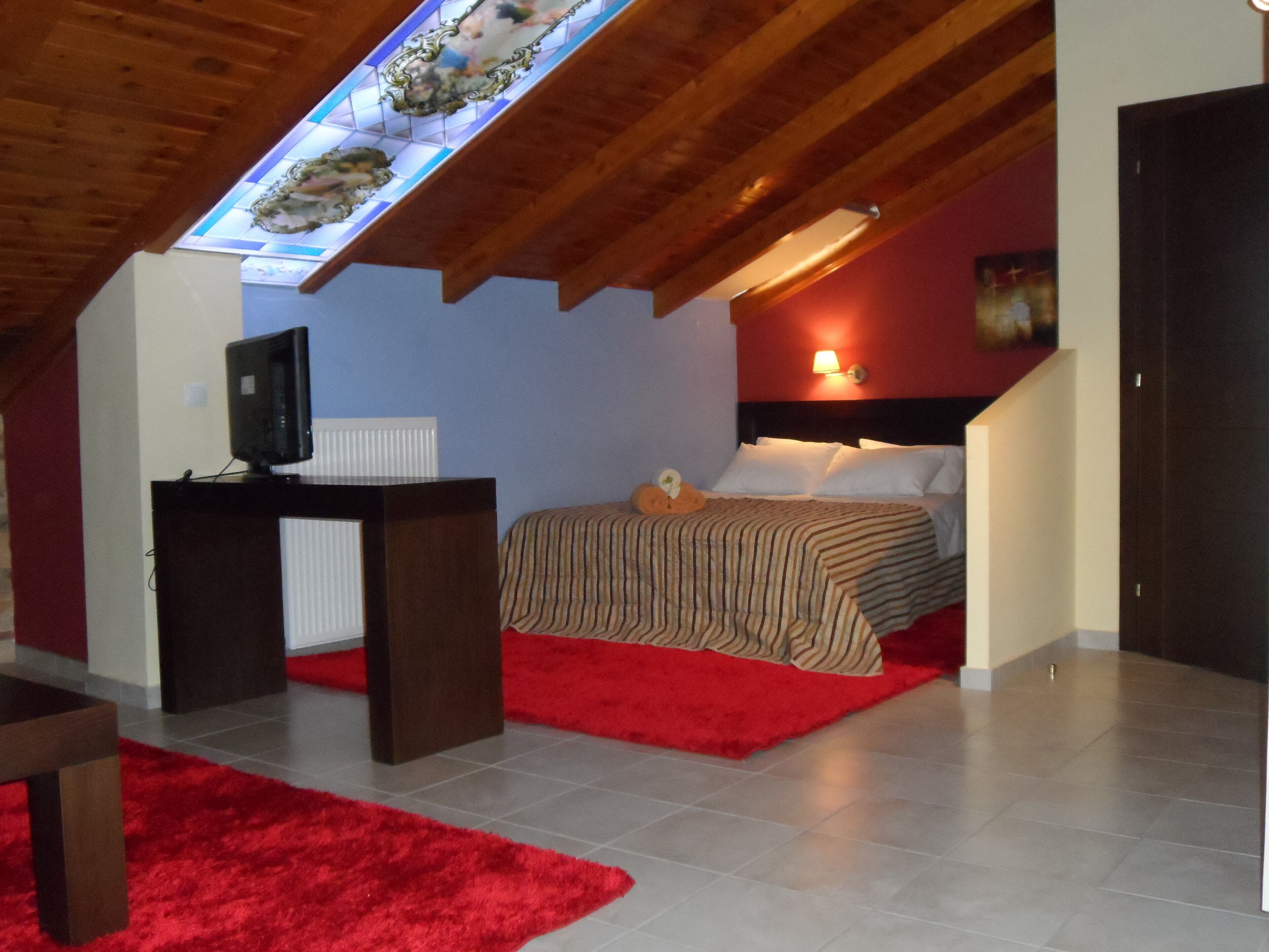 A bedroom with a sloped ceiling, a bed with striped bedding, a red rug, a television on a stand, and a wall-mounted lamp.