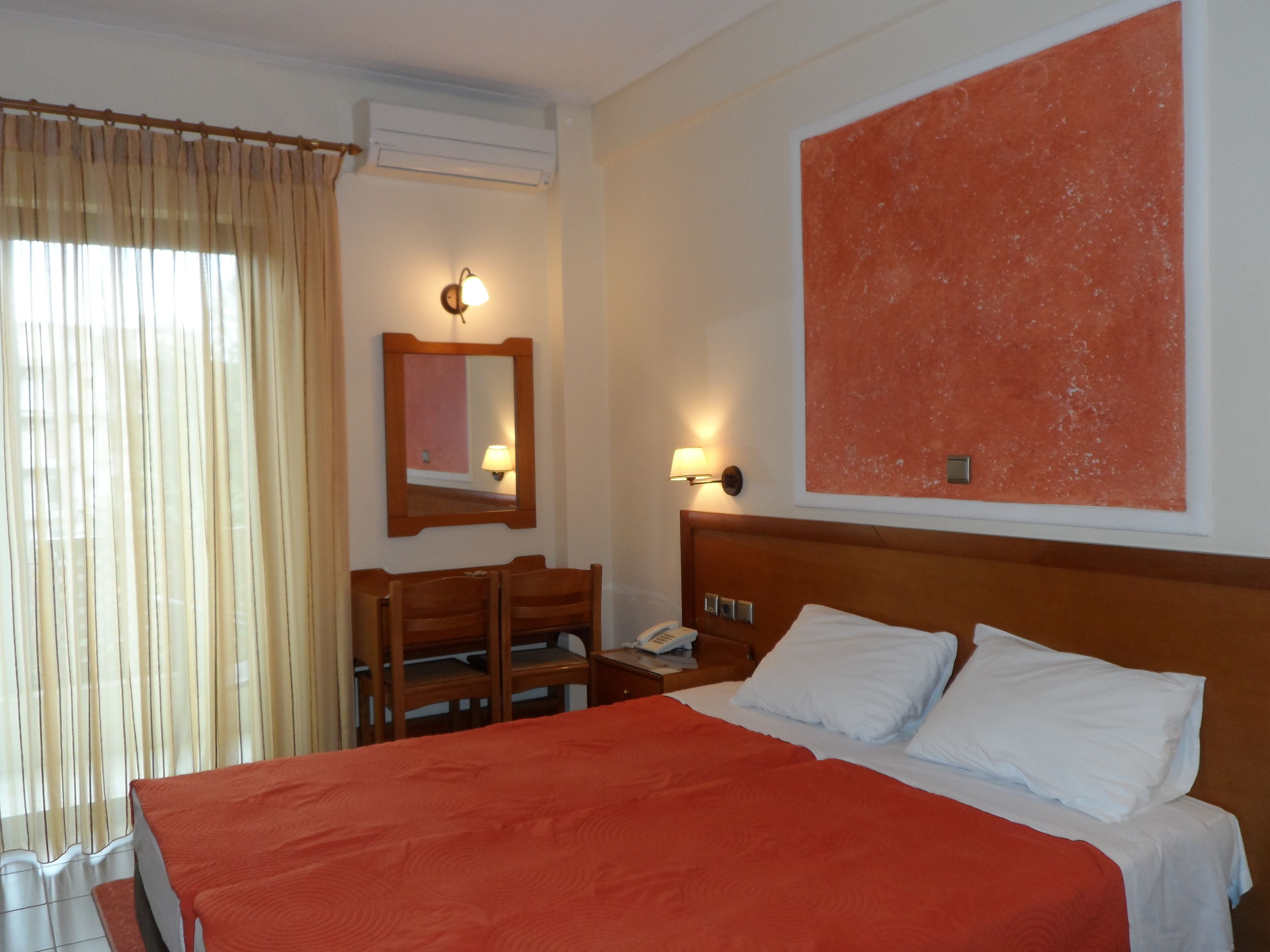 Habitación de hotel con una cama grande, un escritorio con teléfono, un espejo y dos lámparas fijadas a la pared.